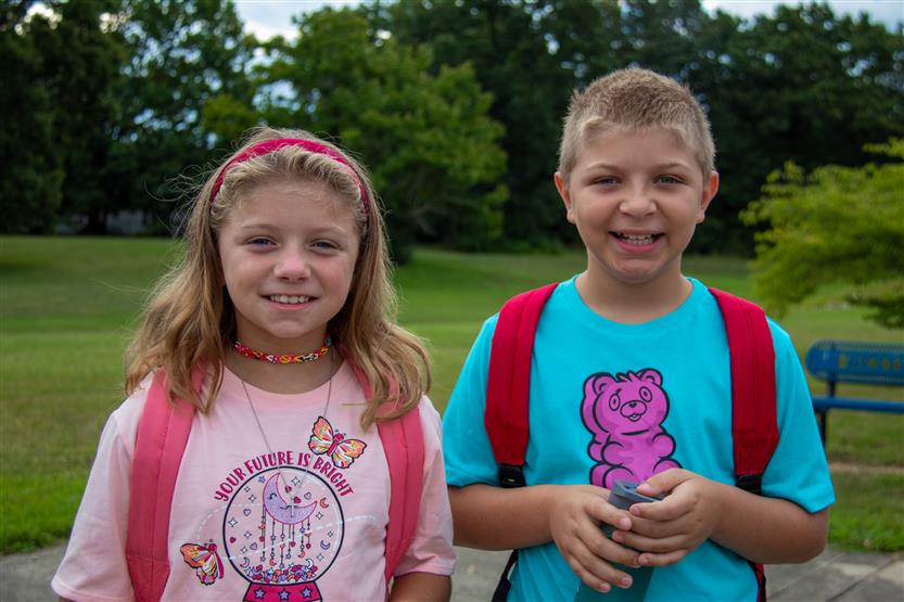 Two students, a girl wearing pink and a boy wearing blue, smile